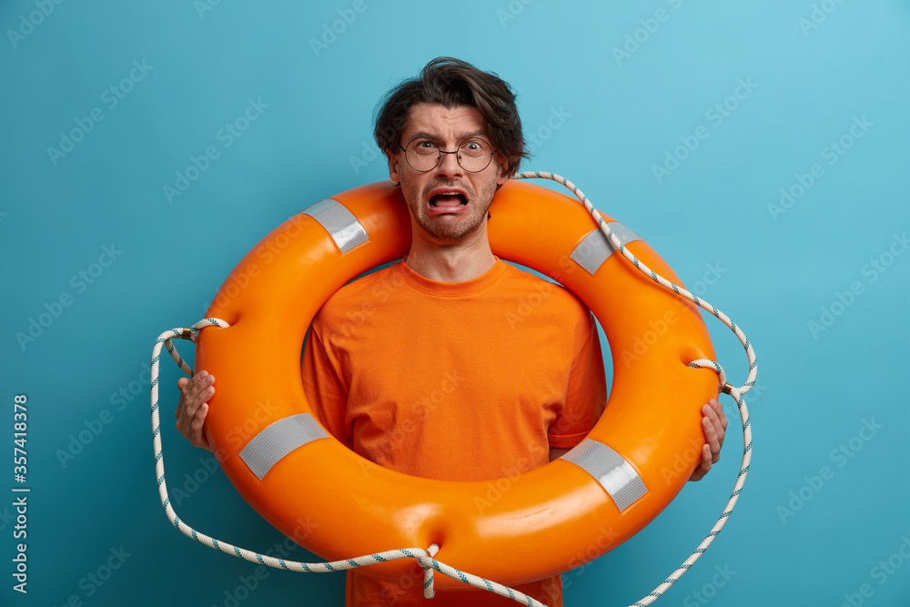 Depressed man lifeguard cries with panicking expression, poses with