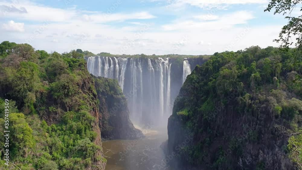 Panorama view at Victoria Falls, Zambia, the largest Waterfall with a blue Sky, and steam in the Air Panorama view at Victoria Falls, Zambia, the largest Waterfall with a blue Sky, and steam in the Air