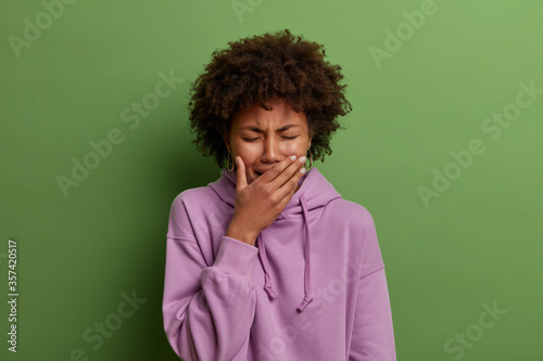 Emotional burnout. Depressed miserable woman sobs and whins from despair, has serious problem, cannot control her emotions, covers mouth, feels distressed and upset, wears casual purple hoodie