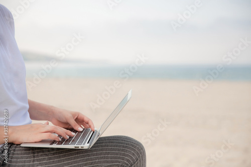 Close up of woman's hands typing on laptop with beach and sea on the background.