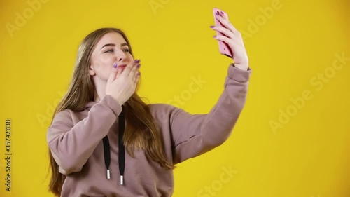 Wallpaper Mural Portrait of cool cheerful woman holding smart phone in hand shooting selfie isolated on yellow background. Torontodigital.ca