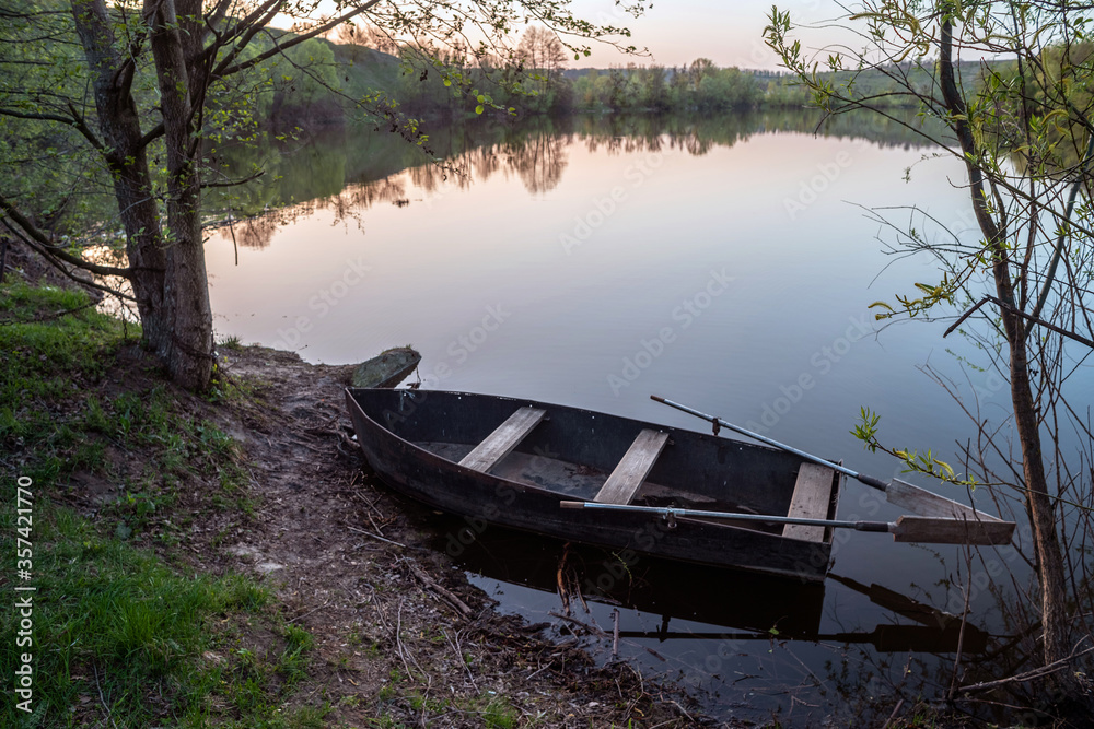 Obraz premium Small boat with oars near the riverbank at sunset. Selective focus.