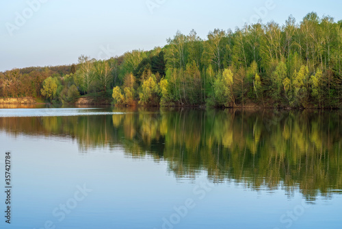 Covered with deciduous trees river with clean water. Landscape with blue water and sky.