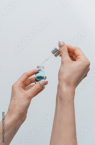 Female hands and bottle with essential oil and pipette on gray background