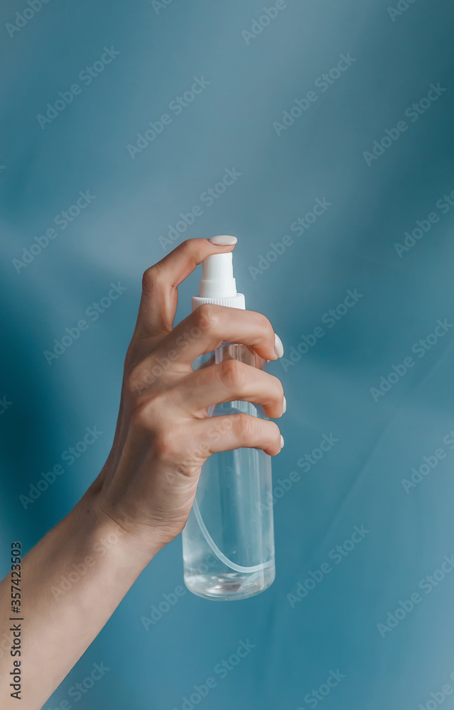 Female hand with bottle of antiseptic gel isolated on blue. Antibacterial spray for hands antiseptic.