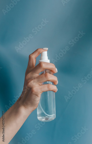 Female hand with bottle of antiseptic gel isolated on blue. Antibacterial spray for hands antiseptic.