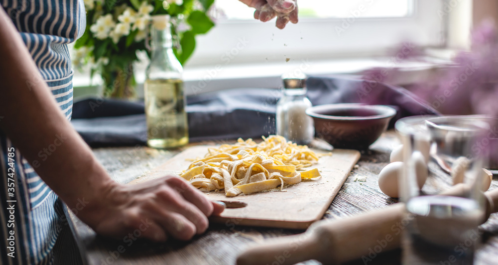 Woman is carefully sprinkling flour on fresh homemade noodles. Concept of cooking handmade pasta in a cozy atmosphere