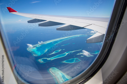 Airplane window with beautiful Maldives island view. Luxury summer holiday travel tourism background, view from airplane window. Atolls and islands with amazing tropical sea