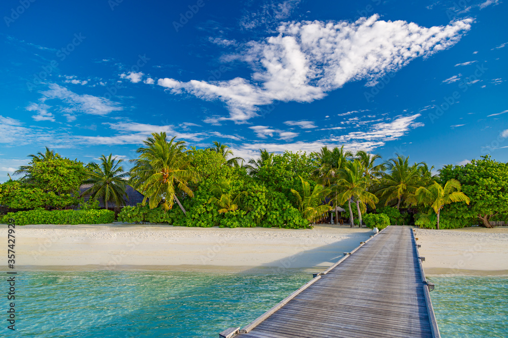 Fototapeta premium Exotic island paradise. Travel, tourism or vacations concept. Tropical beach resort, long jetty with palm trees over white sand, blue sky. Luxury summer holiday vacation landscape