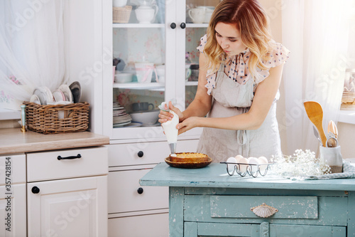 Cute woman immersed in cooking squeesing whipping cream on a small cake