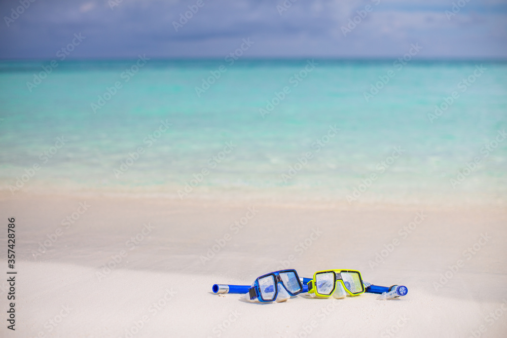 Obraz premium Diving goggles and snorkel gear on sandy beach. Scuba diving and snorkeling. Two snorkel on white sand beach background. Tropical nature landscape blurred sea view. Summer couple recreational activity