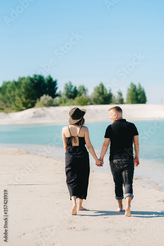 young couple a guy with a girl in black clothes are walking on the white sand