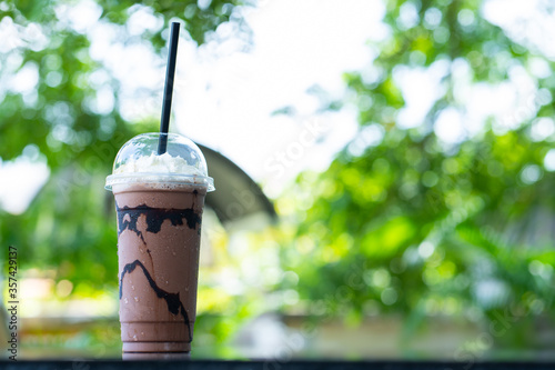 Cold cocoa in plastic glasses with the backdrop bokeh of green leaves sunlight. © 249 Anurak