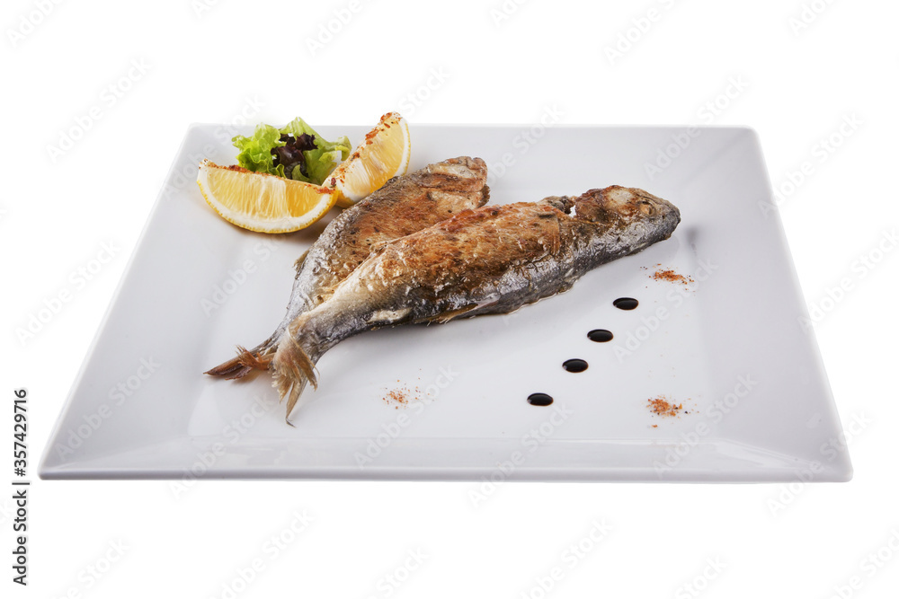 Grilled mackerel rests on a white plate. The fish is decorated with lemon. Grilled mackerel rests on a white plate. The fish is decorated with lemon.