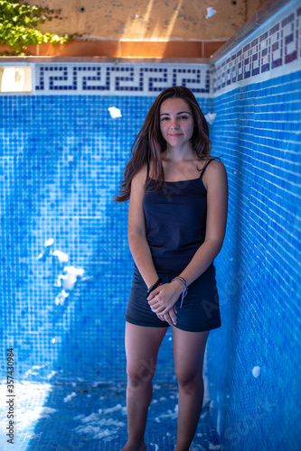 Young pretty woman with black hair standing in an empty swimming pool with blue background thinking and smiling with foam flying