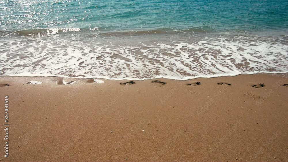 Waves dissolve human footprints in the yellow sand Waves dissolve human footprints in the yellow sand