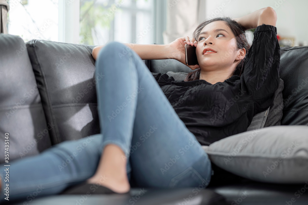 Photo of young asian woman in casual wear using cell phone while lying on sofa in bright apartment. Photo of young asian woman in casual wear using cell phone while lying on sofa in bright apartment.