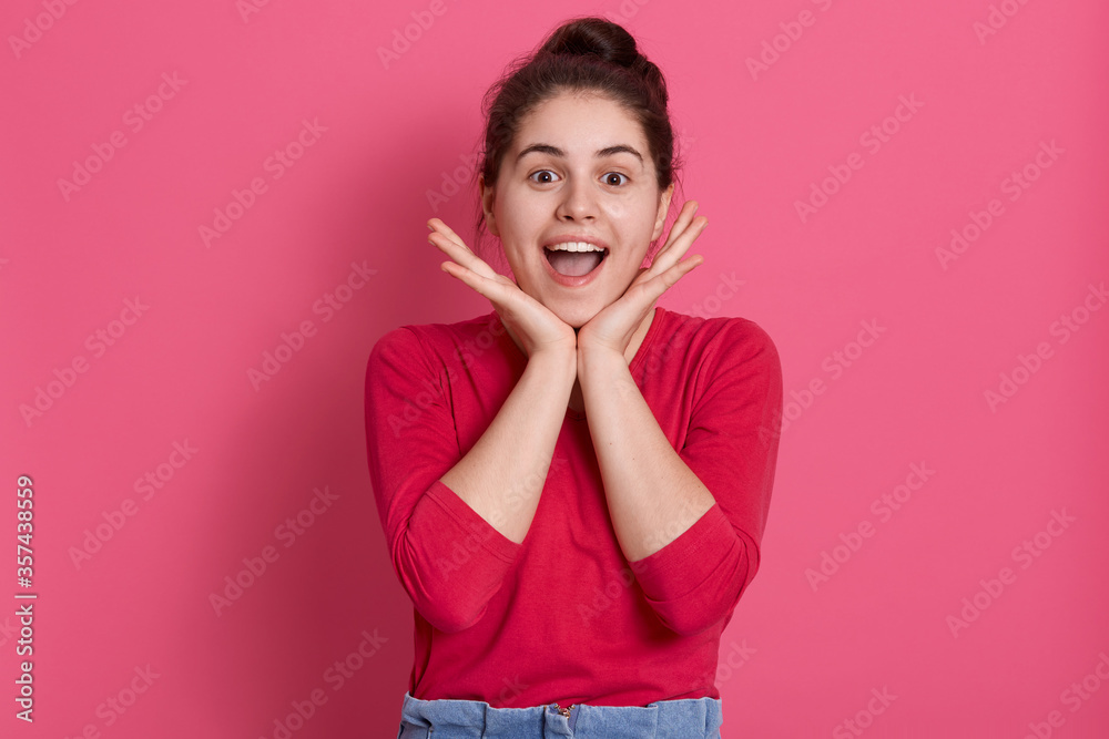 Happy smiling female wearing casual attire looking directly at camera with excited facial expression, keeping palms under chin, yelling happily against pink background. Happy smiling female wearing casual attire looking directly at camera with excited facial expression, keeping palms under chin, yelling happily against pink background.
