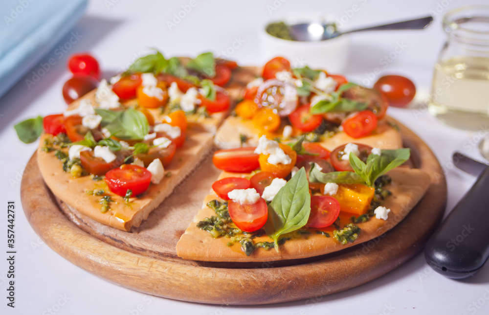 Homemade pizza with cherry tomatoes, fresh green basil and feta cheese. Homemade food. Concept for a tasty and hearty meal. Wooden background. Close up. Homemade pizza with cherry tomatoes, fresh green basil and feta cheese. Homemade food. Concept for a tasty and hearty meal. Wooden background. Close up.