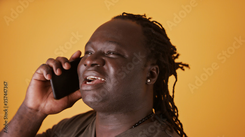 Portrait shot of an african man having a phone conversation. Isolated on the orange background. © CameraCraft