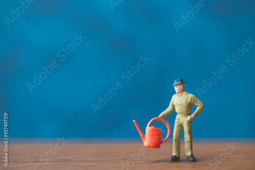 Miniature people gardener standing in front of a blue wall background photo