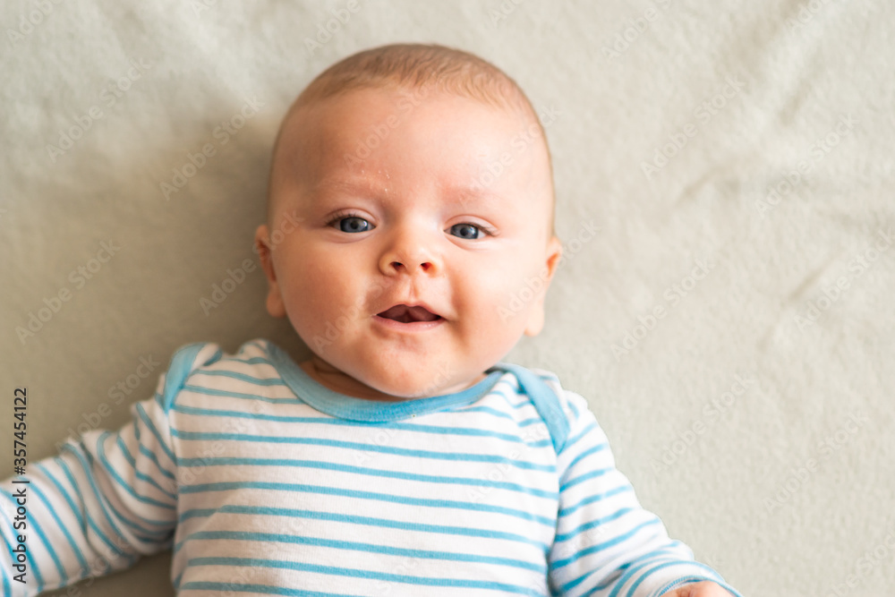 Happy, cheerful baby boy smiling and looking to the camera, lying on grey blanket. Face to face contact with the baby, trying to get his attention.