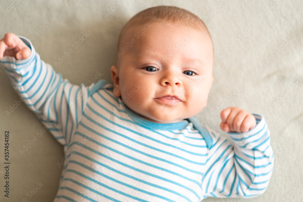 Happy, playful baby boy smiling and waving his arms, lying down in blue stripes bodysuit on grey blanket. Caucasian, blue eyed boy playing Happy, playful baby boy smiling and waving his arms, lying down in blue stripes bodysuit on grey blanket. Caucasian, blue eyed boy playing