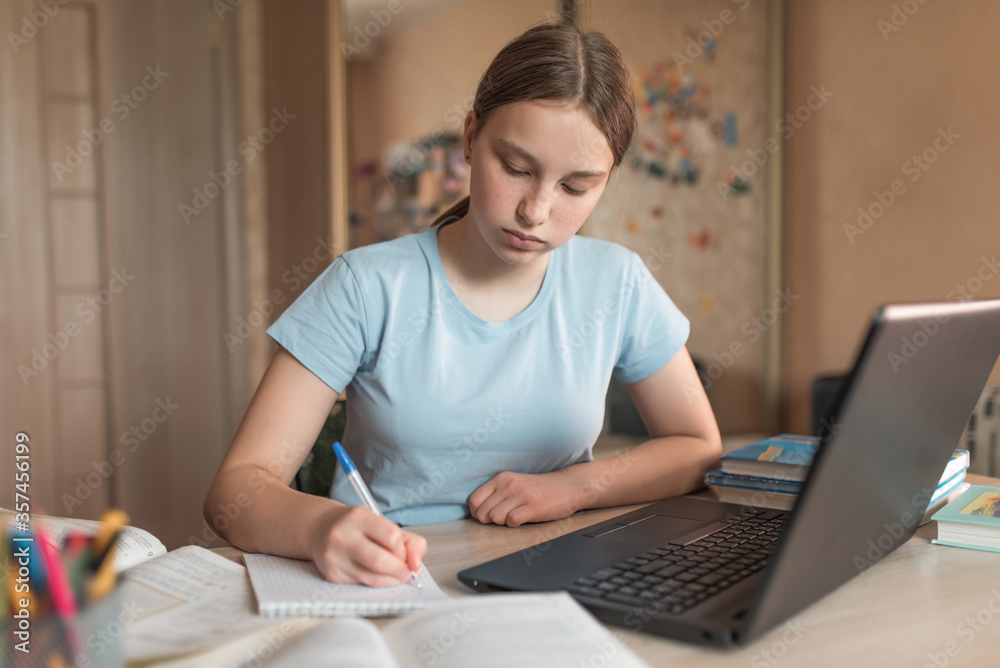 Teen girl does homework, writes lessons in a notebook, notebook monitor, e-learning and online lessons, distance learning. Social networks video call, watching a teacher’s lecture video on Internet. Teen girl does homework, writes lessons in a notebook, notebook monitor, e-learning and online lessons, distance learning. Social networks video call, watching a teacher’s lecture video on Internet.