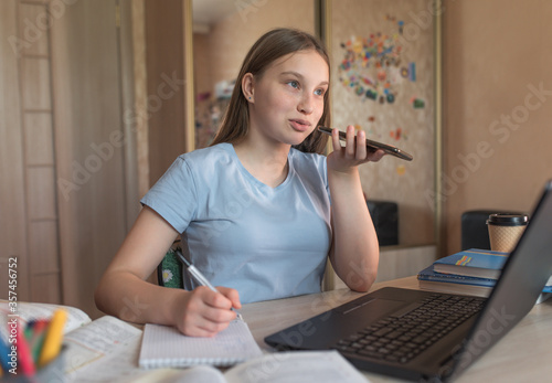 Teen girl doing homework, recording a voice message, making phone call, laptop monitor, e-education online lessons, distance learning. Social networks, watching a teacher’s lecture on Internet.