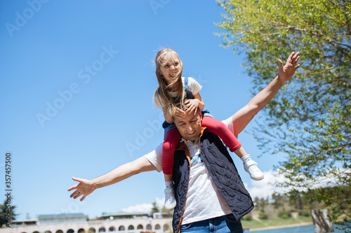 Daughter is sitting on her father's shoulders smiling and having fun outdoor. Copy space.