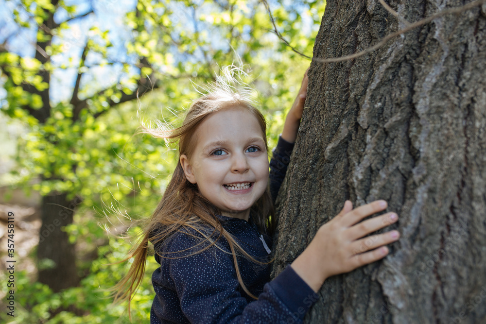 A little girl standing near tree and smiling. Close up. Copy space. Lifestyle concept. A little girl standing near tree and smiling. Close up. Copy space. Lifestyle concept.