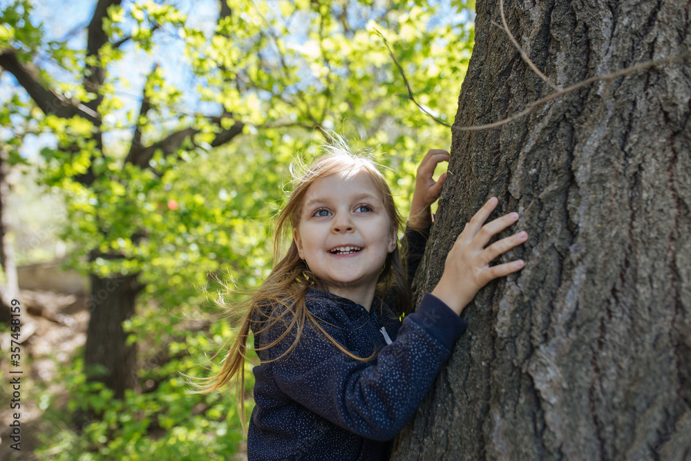 A little girl standing near tree and smiling. Close up. Copy space. Lifestyle concept. A little girl standing near tree and smiling. Close up. Copy space. Lifestyle concept.