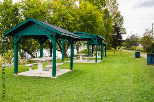 Empty picnic tables under wooden shelters in a riverside public park on a cloudy autumn day. NB, Canada.