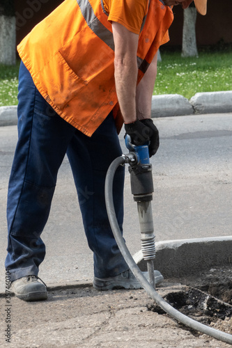 Dismantling of the road surface. A road worker with tension is hammering the asphalt with a jackhammer. Vertical image.
