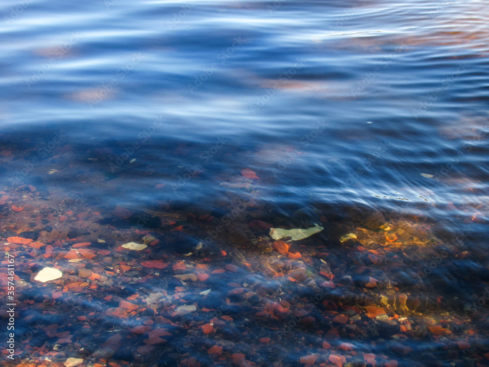 rare small waves on calm blue water. Small stones Shine through the clear water. rare small waves on calm blue water. Small stones Shine through the clear water.