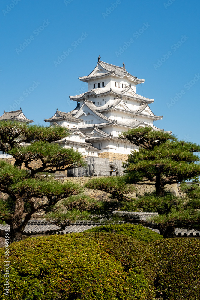 Vertical portrait view of snow white Himeji Castle complex in a crystal blue sky background and green tress in front, Japan. Vertical portrait view of snow white Himeji Castle complex in a crystal blue sky background and green tress in front, Japan.