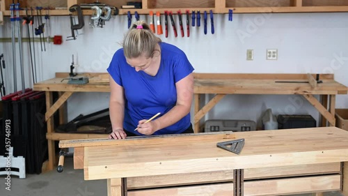 Female caucasian young adult woodworker measuring and marking wood with a metal yardstick and triangle.
