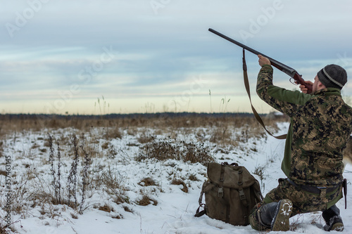 Hunting for wild animals. Hunter with a gun on the field on a cloudy sky background