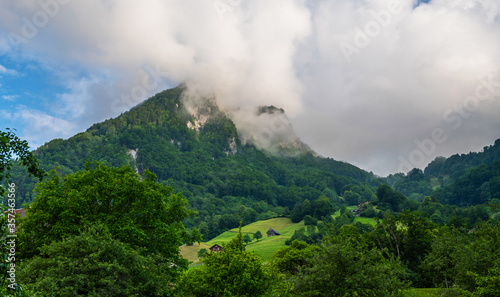 Mountains landscape. Beautiful view of Swiss mountains. Hazy blue mountains covered by fog. Alpine houses, meadows on the slopes. Switzerland, Europe.