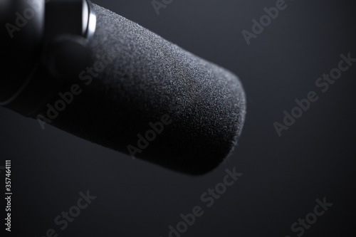 Black microphone with windscreen on black background. For singing, recording, audio work, audio books or narration. Dramatic closeup of windscreen.
