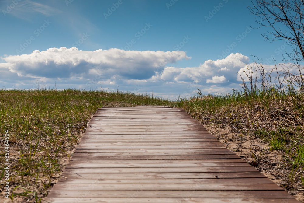 Clouds and horizon on the background of the road to the beach, lined with wooden boards on the sand and grass.