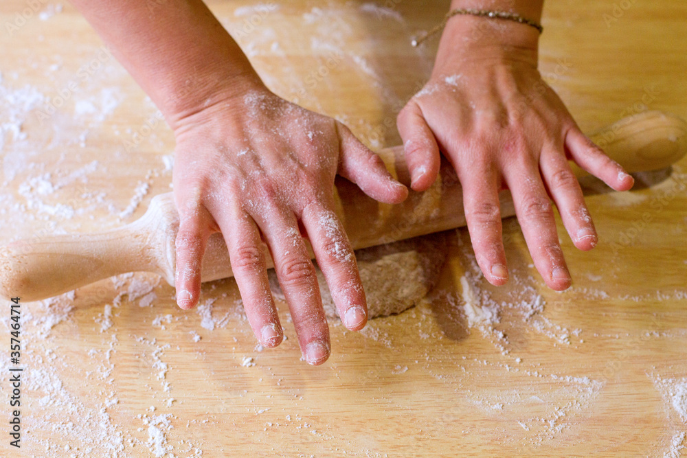 Close up of female hands using a wooden rolling pin.