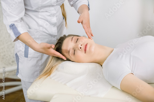 Cropped image of hands of young female cosmetologist examining face and hair of pretty blond girl, relaxed lying on the couch. Cosmetology and beauty center, spa procedures. Planning beauty treatment