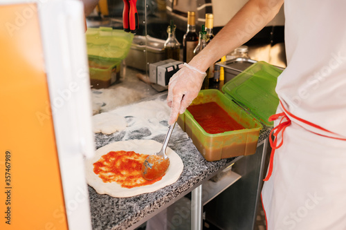 The process of making pizza. The cook prepares the dough for Italian pizza and covers it with tomato paste.