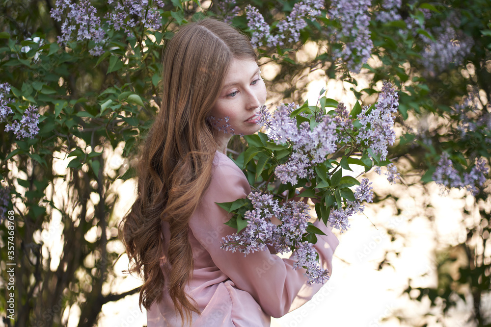 A young girl with light long wavy hair, standing in the leaves of trees on the girl's cheeks lilac petals A young girl with light long wavy hair, standing in the leaves of trees on the girl's cheeks lilac petals