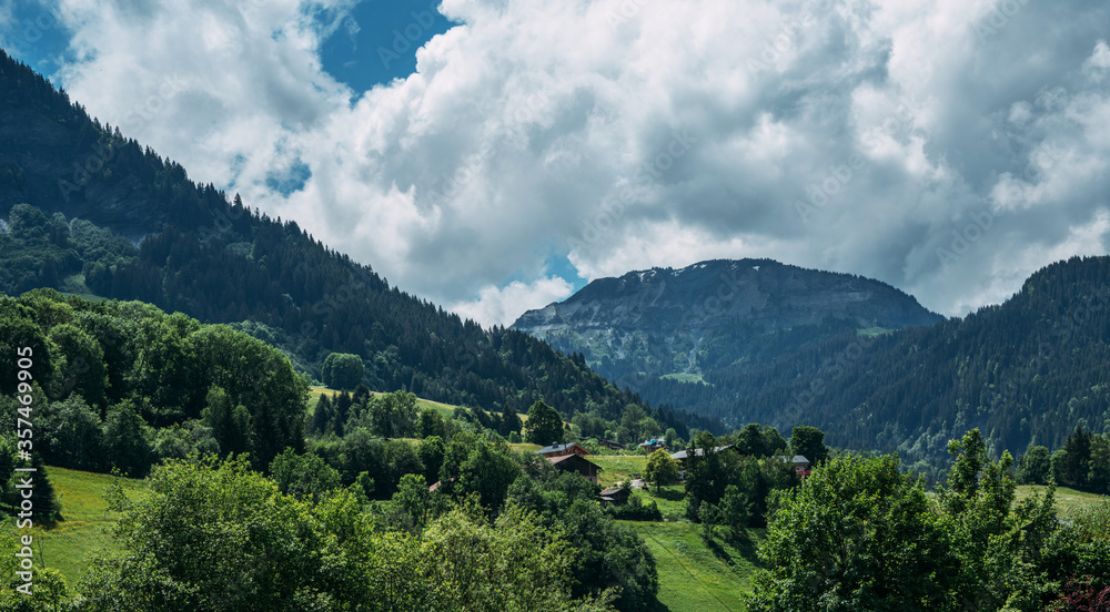 Amazing summer panorama with mountains, small village, green meadows and cloudly blue sky in Swiss Alps. Oberland, Switzerland.