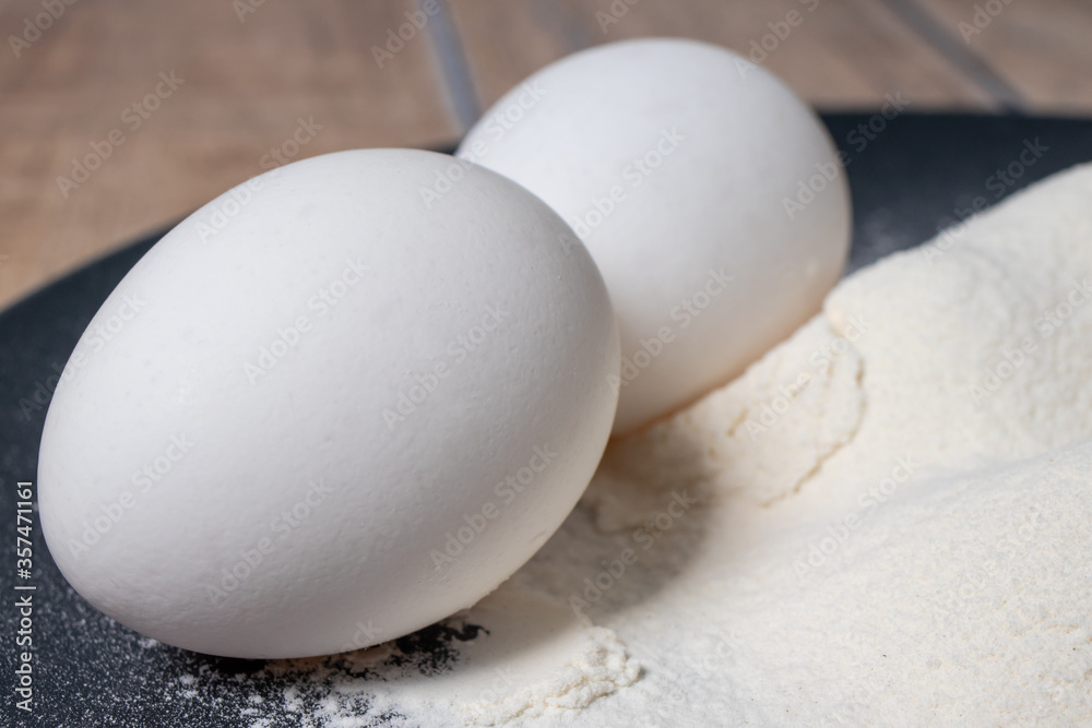 Wheat white flour and eggs on a black plate. Making bread and baked goods. Cooking at home Wheat white flour and eggs on a black plate. Making bread and baked goods. Cooking at home