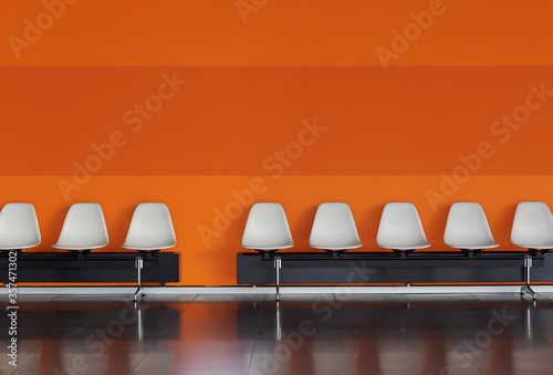 Empty chairs in a row White chairs against the orange wall.