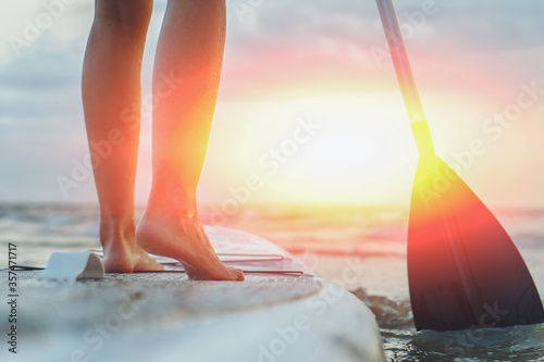Young sexy woman surfer standing on her sup board with a paddle looking to the sunset. Rest at nature concept