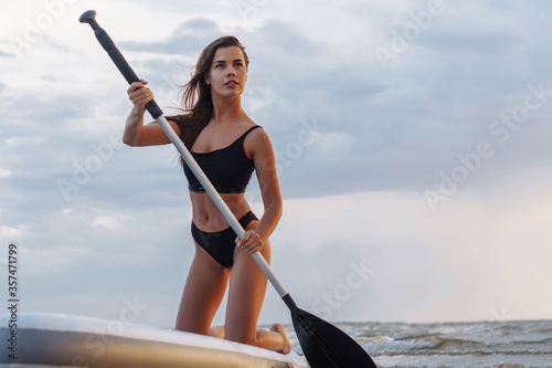 Young sexy woman surfer standing on her sup board with a paddle looking to the sunset. Rest at nature concept